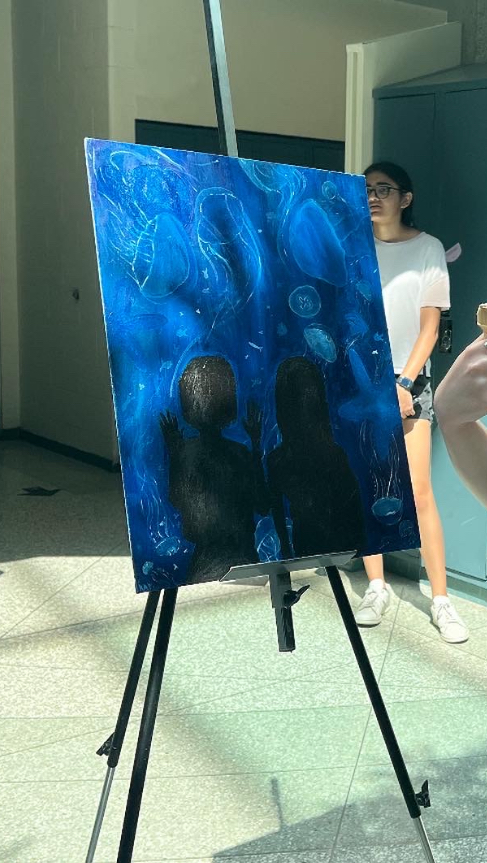 A background blended with different shades of bright blue light up the painting as on top lays a black sihlouette of two girls looking into an aquarium. The jellyfish come in many flowing shapes, they are translucent and white having their tails move with the waves. 